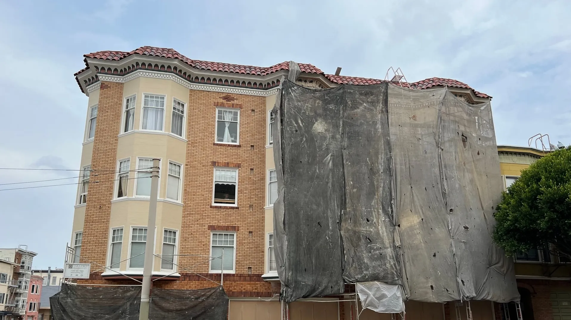 Containment netting and scaffolding on a single elevation of a brick and stucco San Francisco apartment building, with the adjacent finished face already uncovered