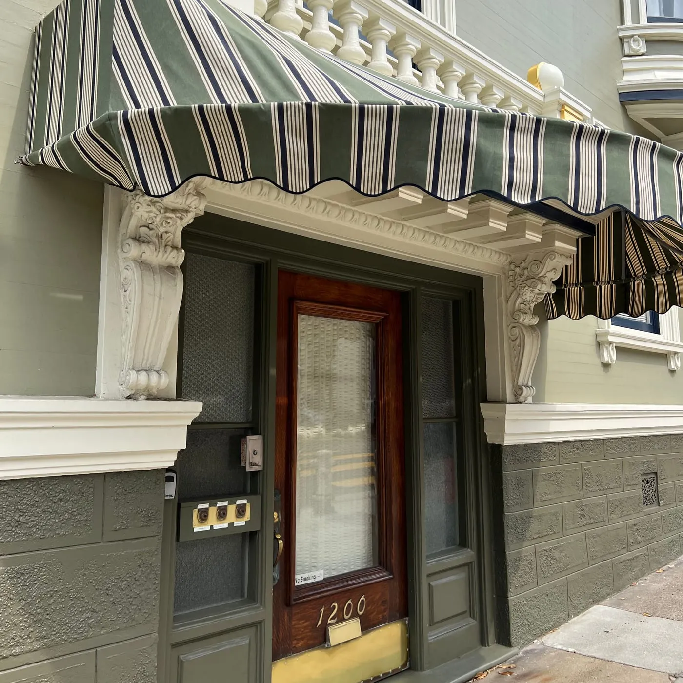 Restored San Francisco entry with a green striped awning, dark green door and gold house numbers